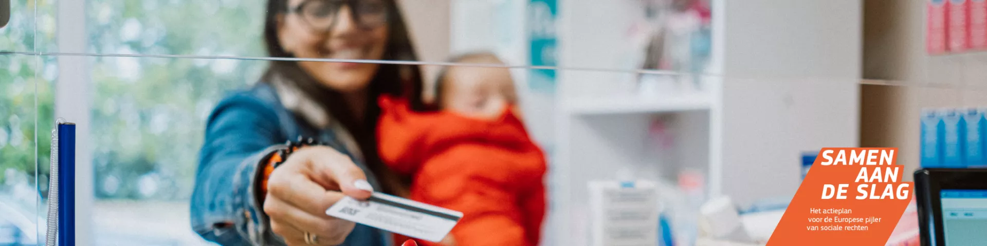 Een vrouw met haar baby op de arm gebruikt een betaalkaart bij een apotheek