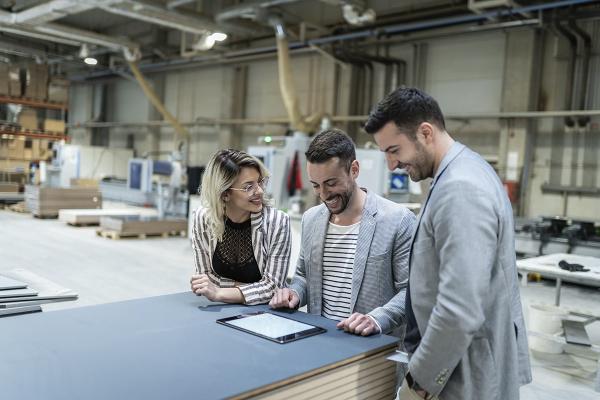 Group of three business partners having a cheerful discussion whilst standing around a workbench and looking at a tablet. 