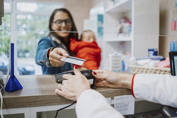 Woman with baby in arms making a payment by card at a pharmacy